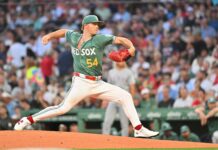 Red Sox Pitching Faces Breakdown After All-Star Break Baseball pitcher in a green Boston Red Sox uniform delivering a pitch on the mound with a crowded stadium in the background.