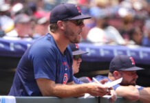 Red Sox Must Ignore Trade Noise And Enjoy This Hot Streak Man in a blue shirt and dark cap signs autographs at a sports event, with a blurred crowd in the background.