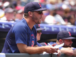 Man in a blue shirt and dark cap signs autographs at a sports event, with a blurred crowd in the background.