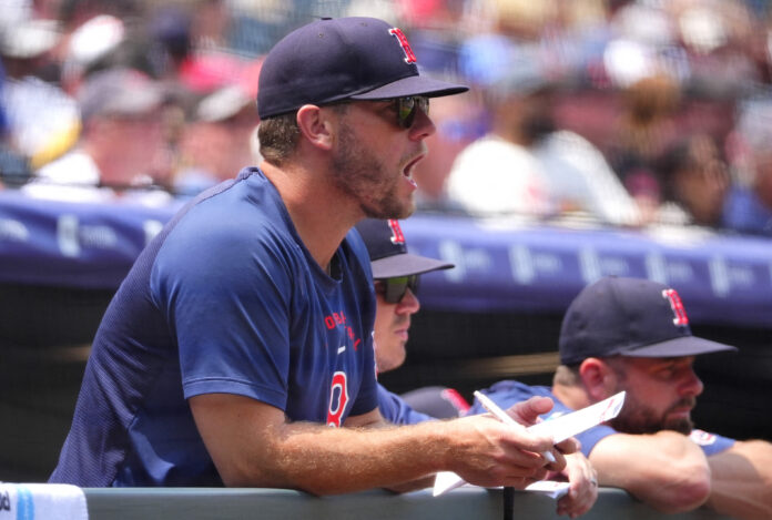 Man in a blue shirt and dark cap signs autographs at a sports event, with a blurred crowd in the background.