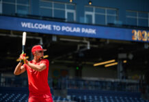 Franklin Arias Delivers Big Night in Worcester Promotion Baseball batter in red uniform and cap swings a bat at Polar Park with a blurred blue sign in the background.