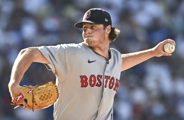 Baseball pitcher in a Boston Red Sox uniform mid-pitch, throwing a ball with his right arm extended and glove on left hand.