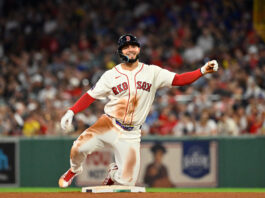 Boston Red Sox baserunner sliding into a base during a game, crowd in the stands blurred in the background.